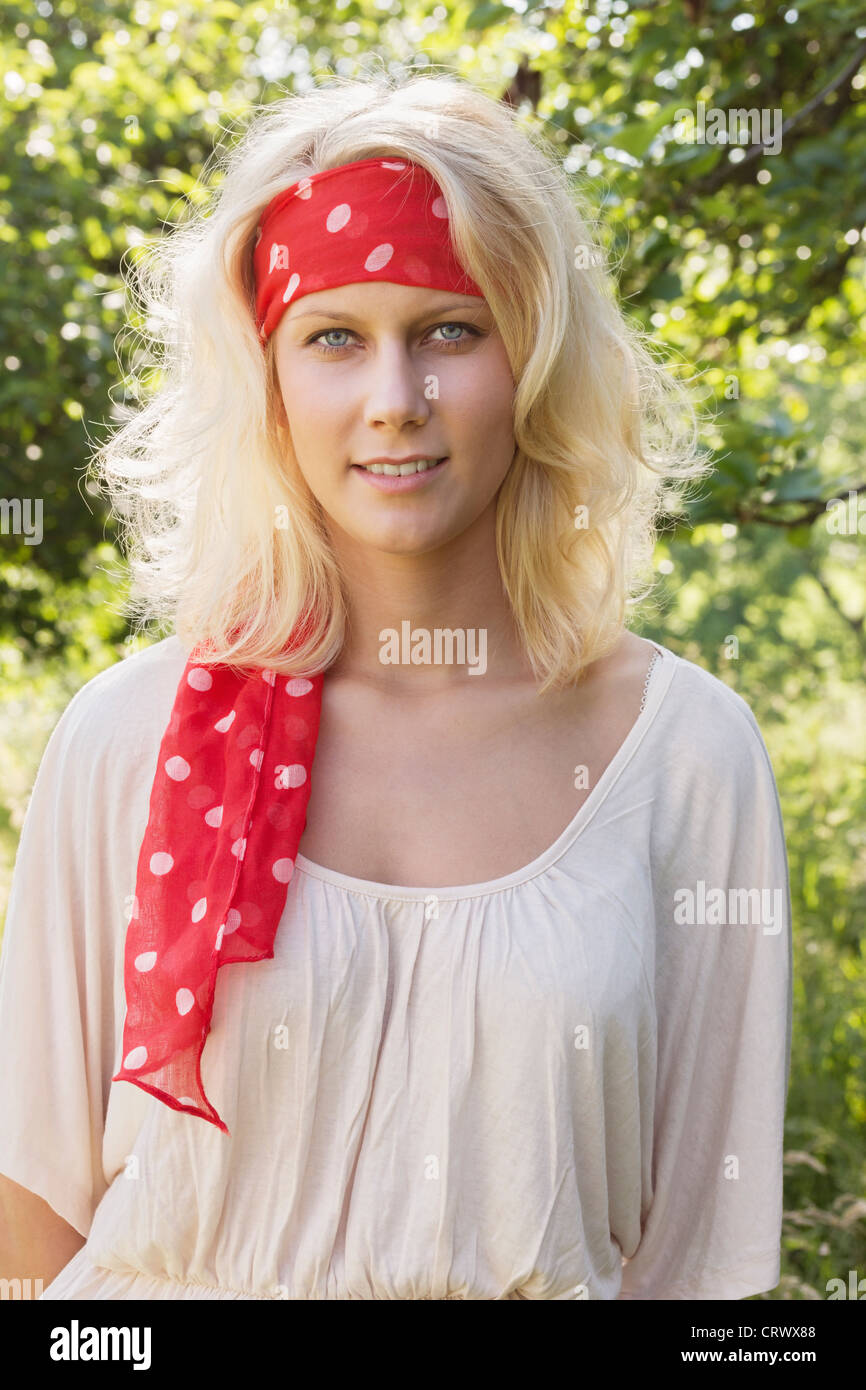 Beautiful young blond teenage girl with bandana looking at the camera. Summer outdoor portrait against a blurry green background Stock Photo