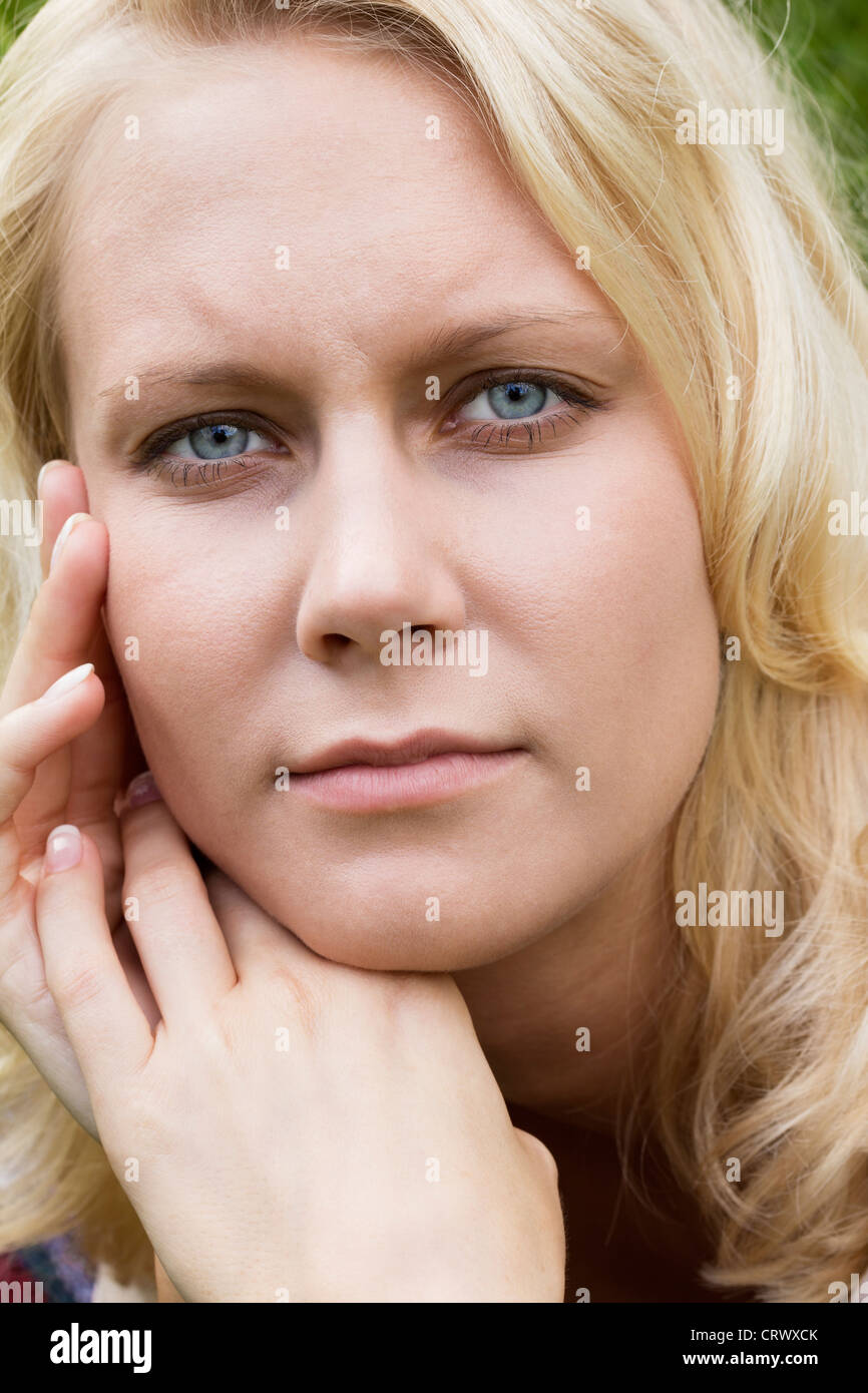 Dreamy young blonde teenage girl lying on meadow looking pensive at the camera. Summer outdoor portrait as close up Stock Photo