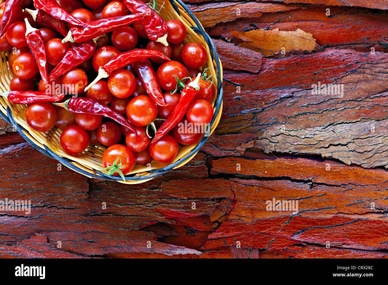 Basket of ripe cherry tomatoes and dried red chillies on rustic stripped bark Stock Photo