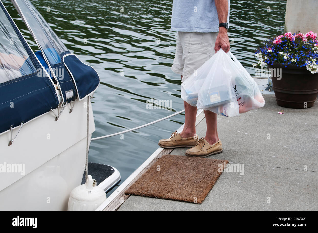 Man stands on marina dock with hands holding full plastic shopping bags filled with provisions. Stock Photo