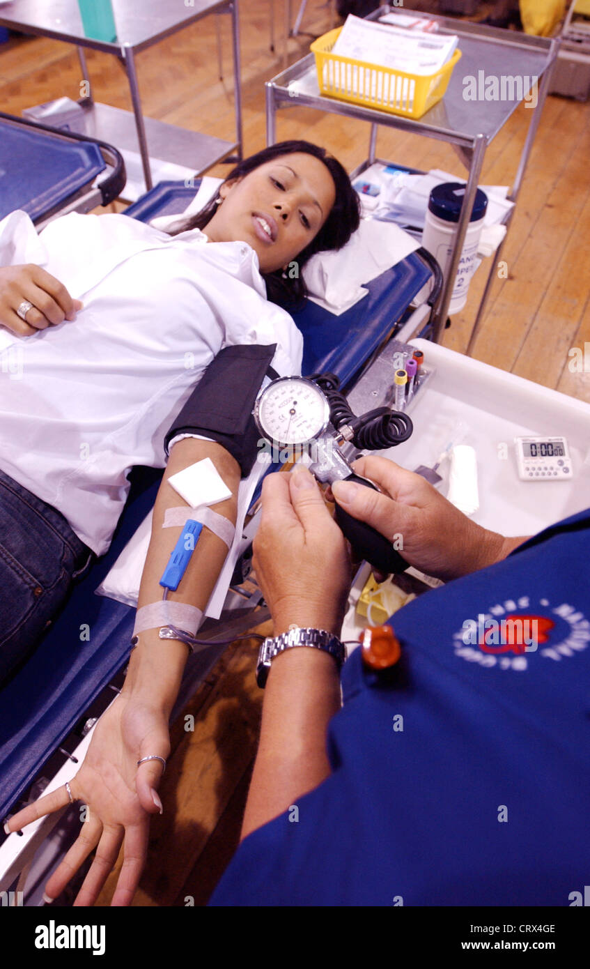 NHS National Blood Service nurse checks the blood pressure of a young female donor with the air pump of a sphygmomanometer. Stock Photo