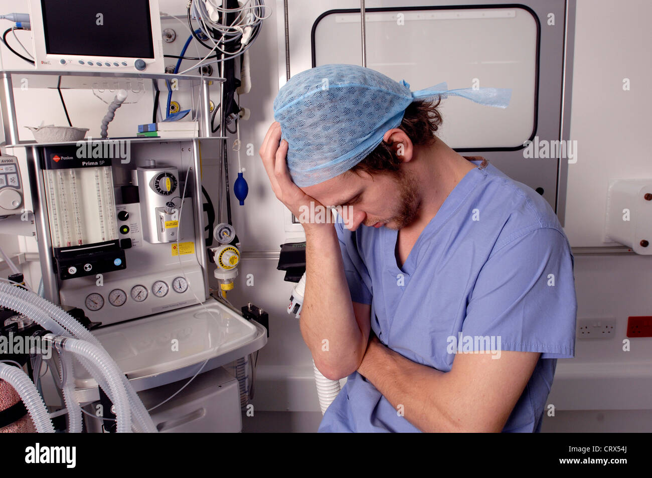 A male doctor, wearing a surgical cap and gown, showing signs of stress and tiredness. Stock Photo