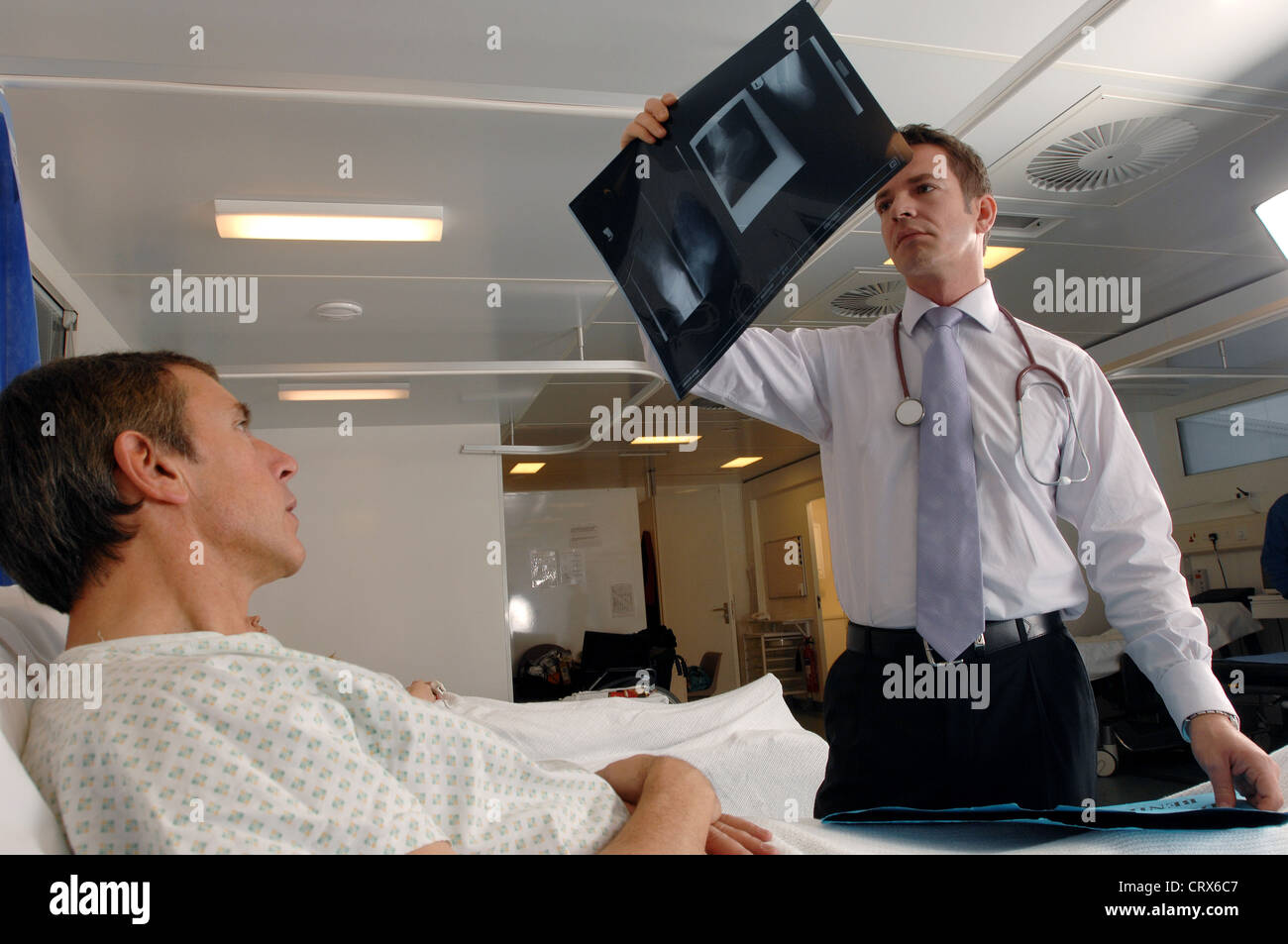 A doctor on his ward round reviews an x-ray during a hospital bedside consultation with his male patient. Stock Photo