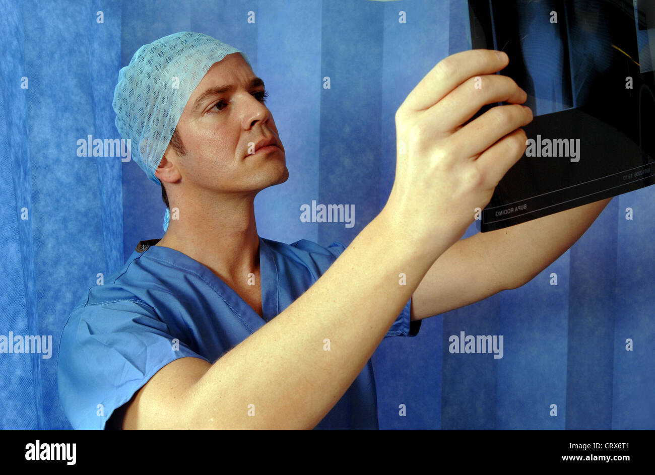 A surgeon wearing blue surgical cap and gown, reviewing a patient's x-ray. Stock Photo