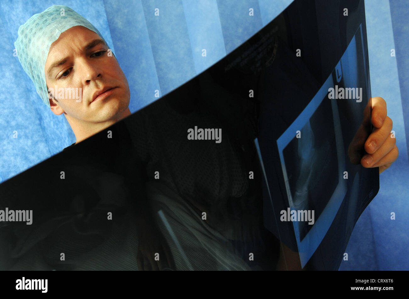 A surgeon wearing blue surgical cap and gown, reviewing a patient's x-ray. Stock Photo