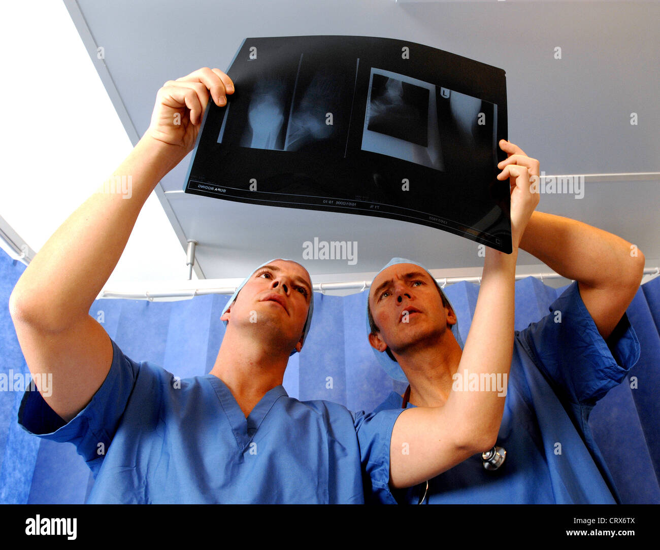 Two surgeons wearing blue surgical caps and gowns, reviewing a patient's x-ray. Stock Photo