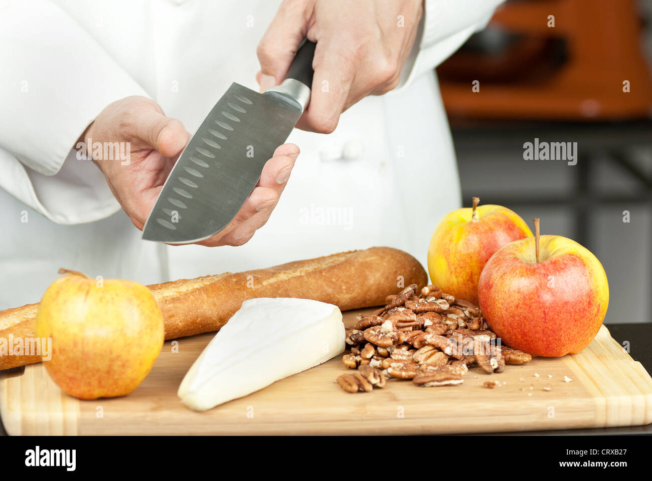 Close-up of a chef testing knife sharpness over a cutting board of apples pecans a baguette and brie. Stock Photo