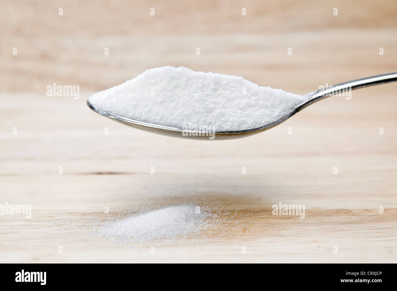 Heaped spoon of caster sugar held over a wooden chopping board Stock