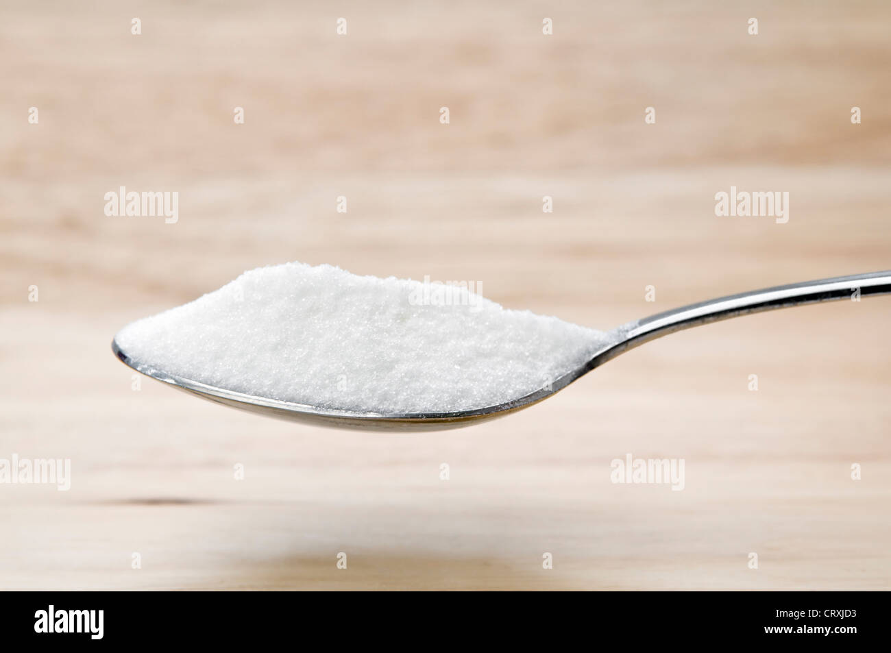 Heaped spoon of castor sugar held over a wooden chopping board Stock