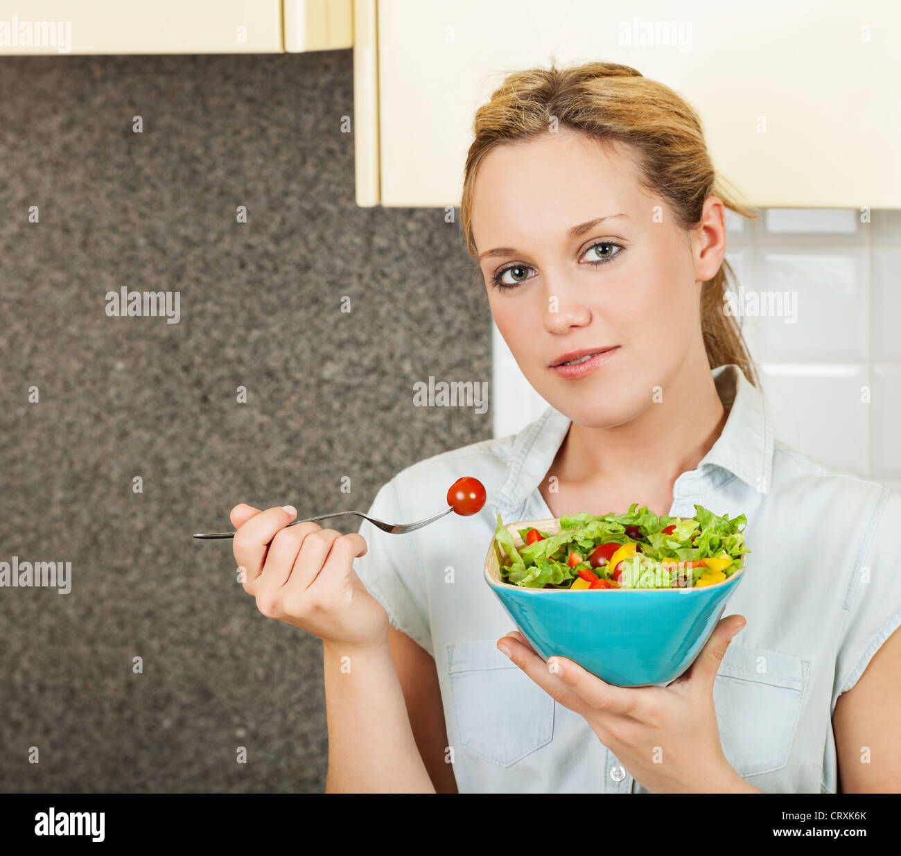 Pretty young woman standing in the kitchen and holding a bowl with salad Stock Photo