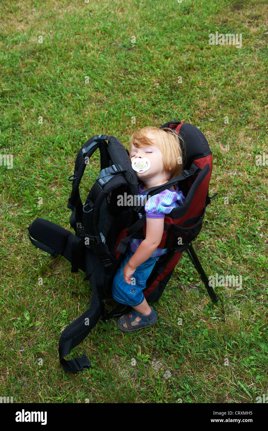 Baby child girl one year old asleep in a backpack baby carrier