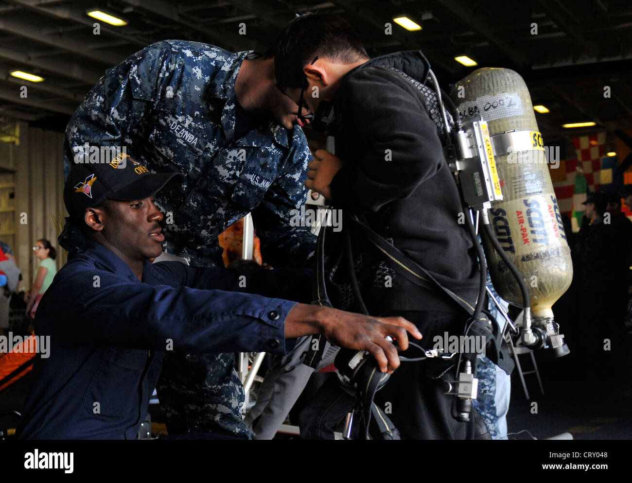 Damage Controlman Fireman Jyree Byrd, assigned to the Engineering DepartmentÕs Damage Control Division, helps a guest don a self-contained breathing apparatus backpack in the hangar bay of the Nimitz-class aircraft carrier USS Carl Vinson (CVN 70) during a friends and family day cruise. Stock Photo