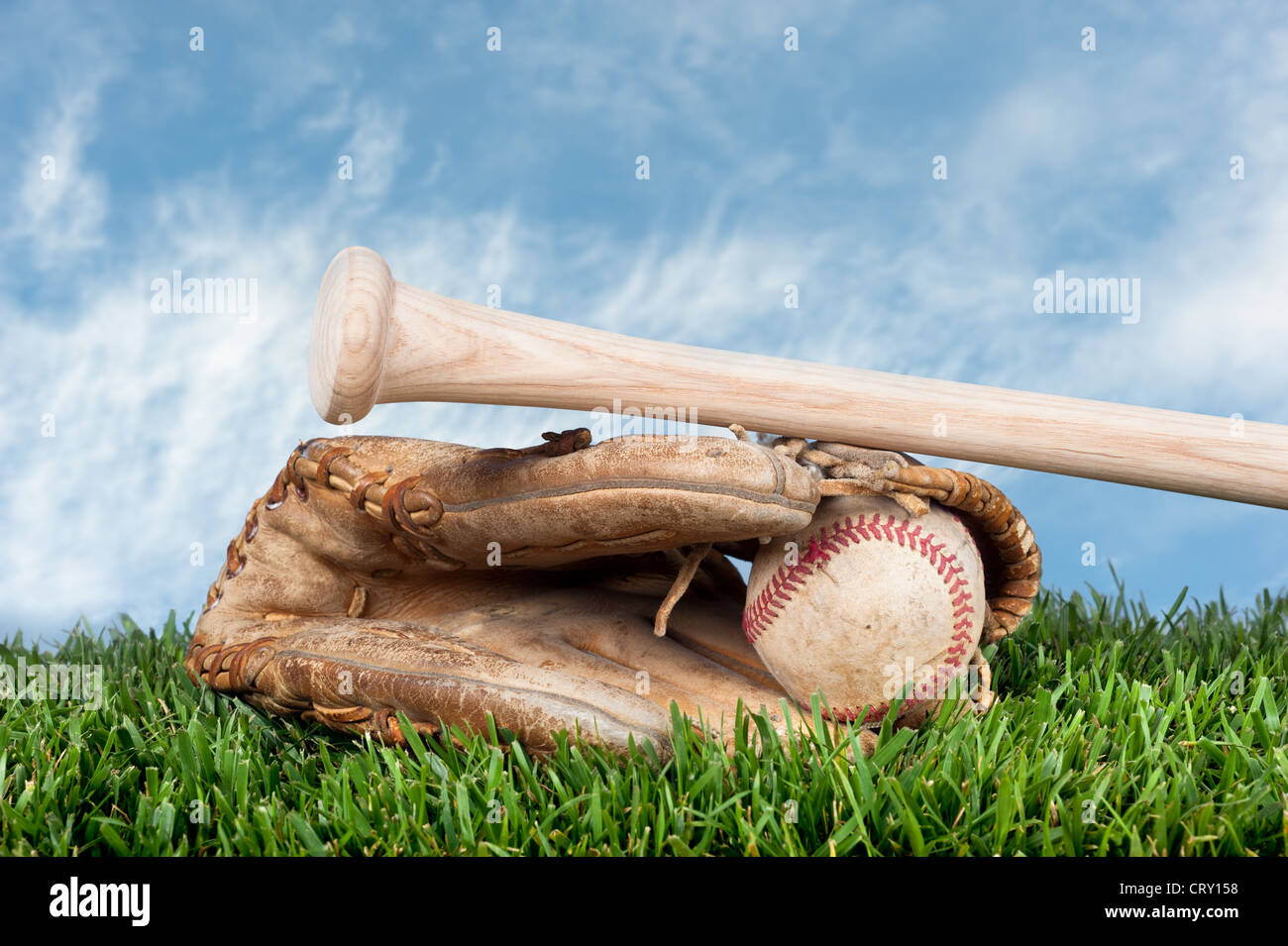 Baseball glove, ball, and bat laying on grass against a blue, lightly