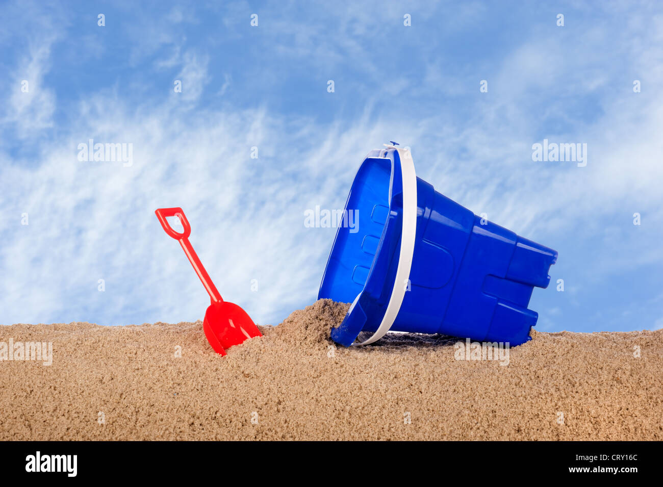 A beach bucket with red shovel in the sand against a blue sky Stock