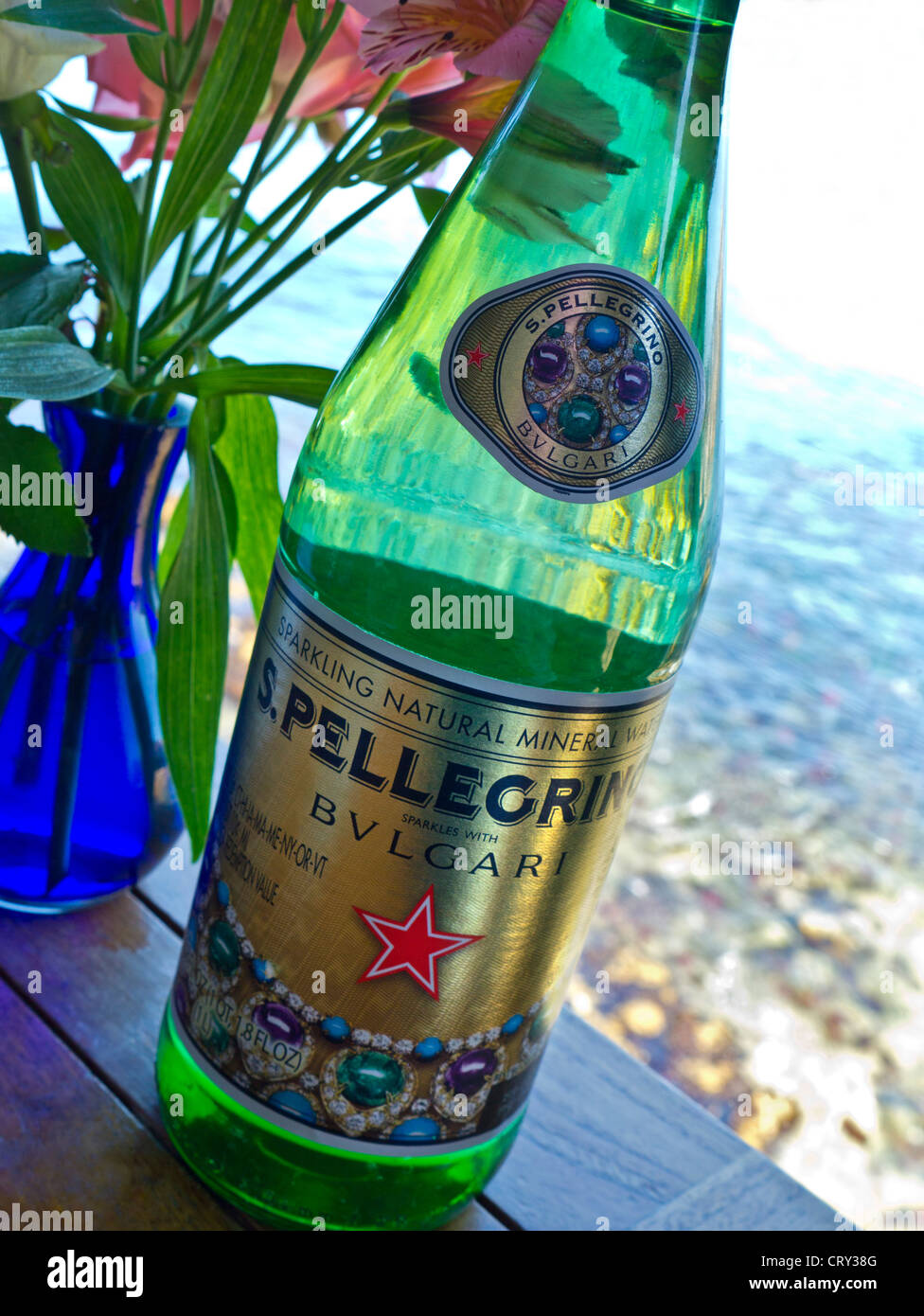 Pellegrino Bulgari luxury bottled water on floral restaurant table with sea view Stock Photo