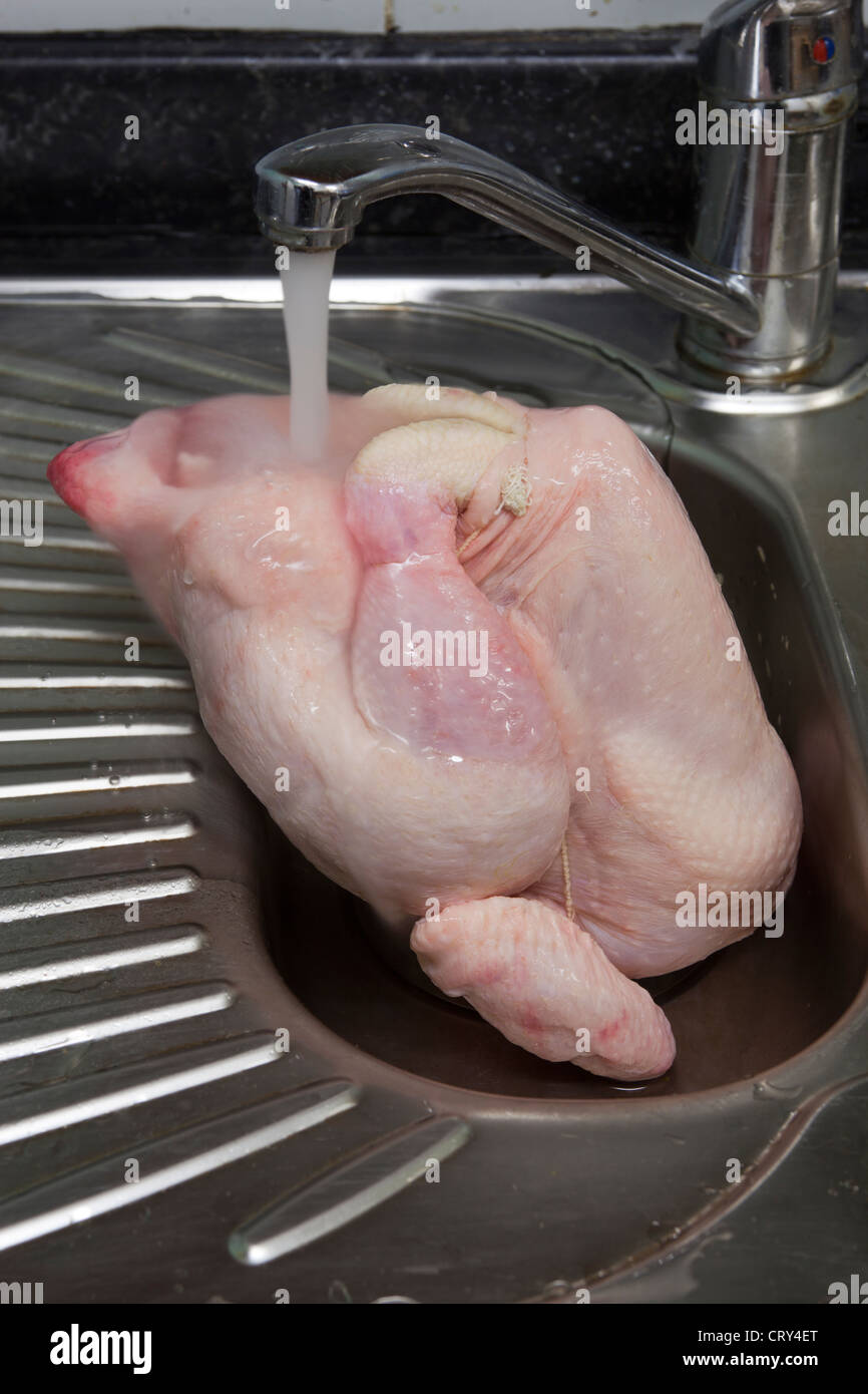 Raw Chicken Under Cold Water Tap In Kitchen Sink Stock Photo