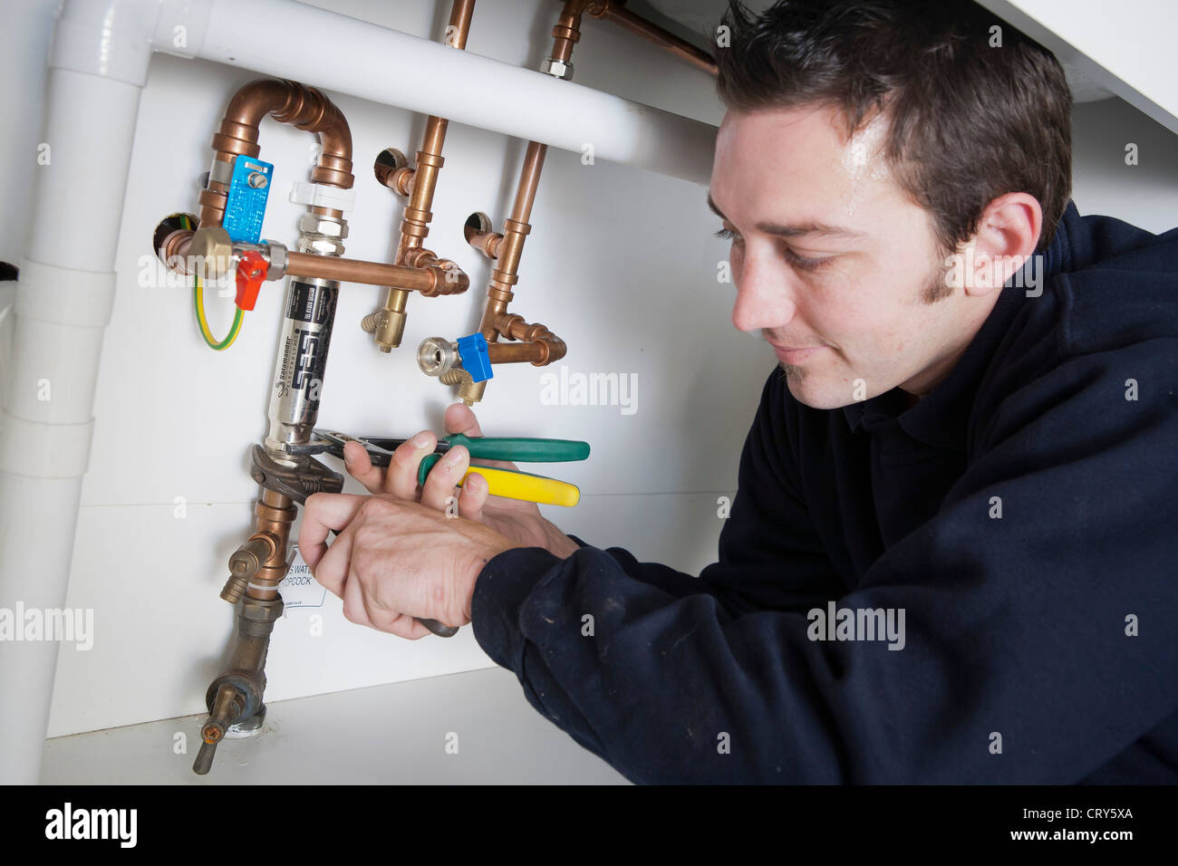 Plummer fixing salamander Sesi electrolytic scale inhibitor to water inlet pipe under the sink Stock Photo