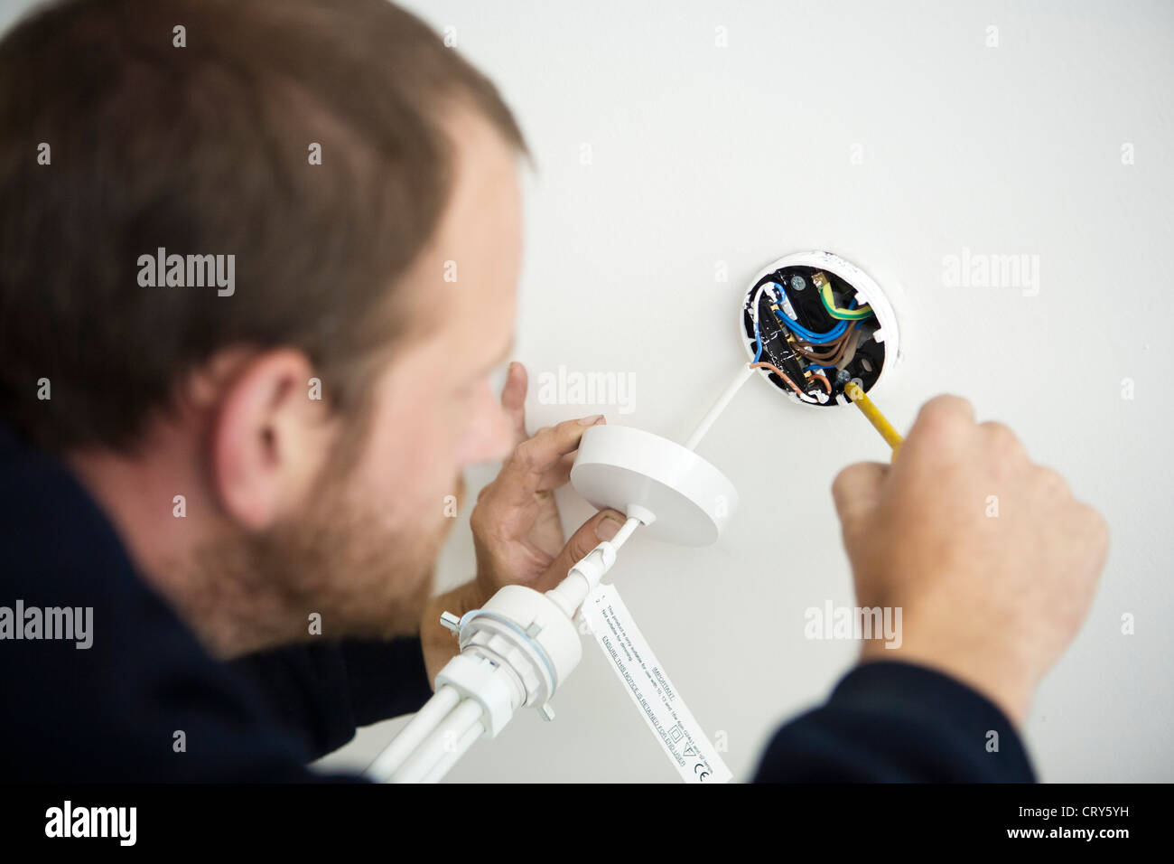 Electrician fixes new light fitting to ceiling fitting Stock Photo Alamy