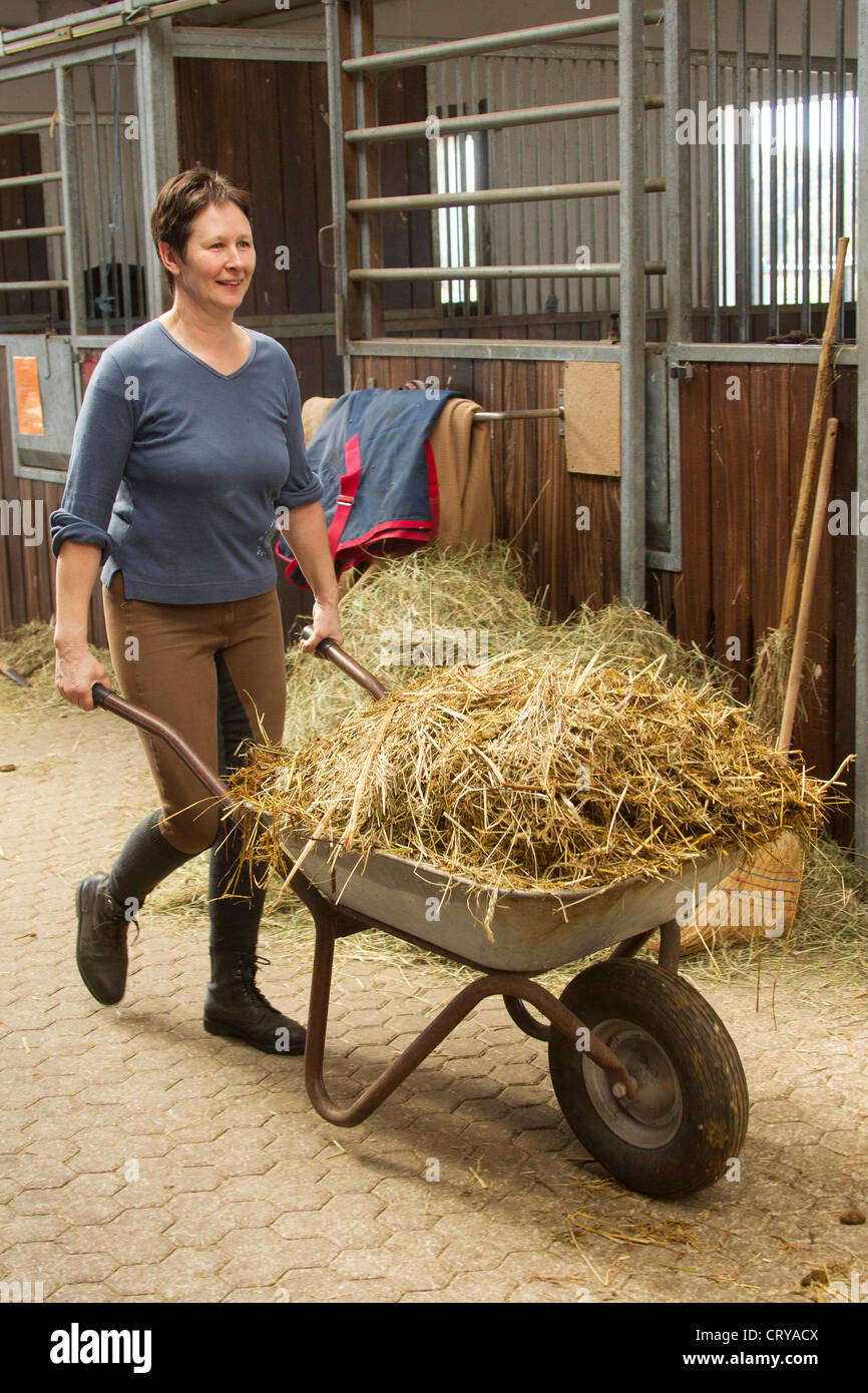Woman pushing a cart with fresh straw in a stable Stock Photo