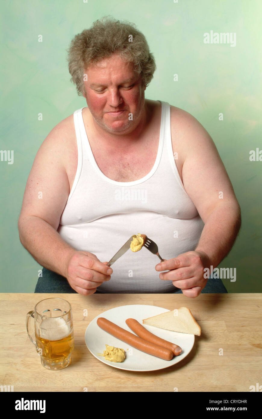 Fat man in undershirt eating two sausages with mustard Stock Photo Alamy