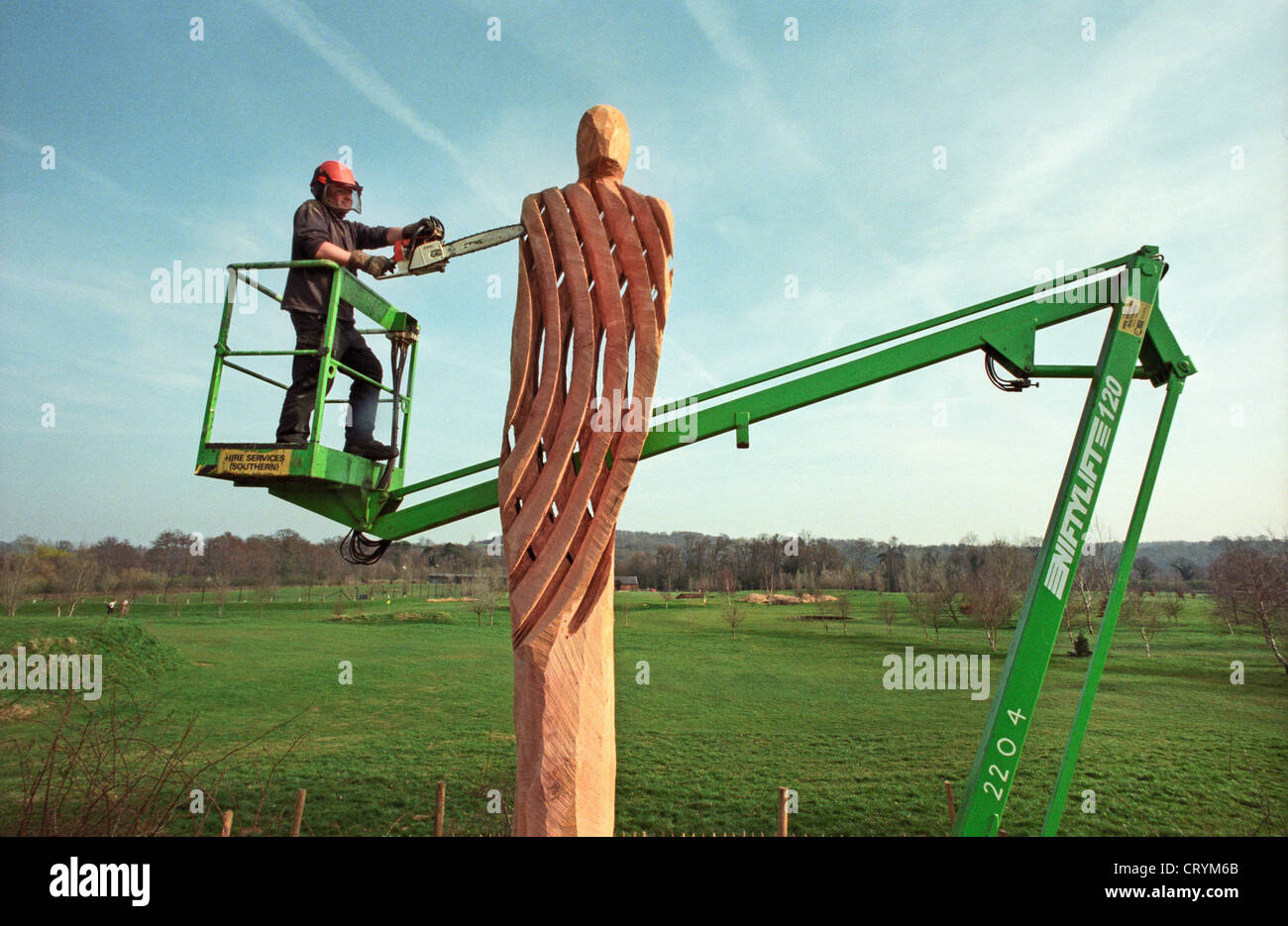 A chainsaw sculptor on the platform of a cherrypicker carving a lattice figure from a dead oak tree in Broadwater Park, Godalming, Surrey, England, UK. Stock Photo