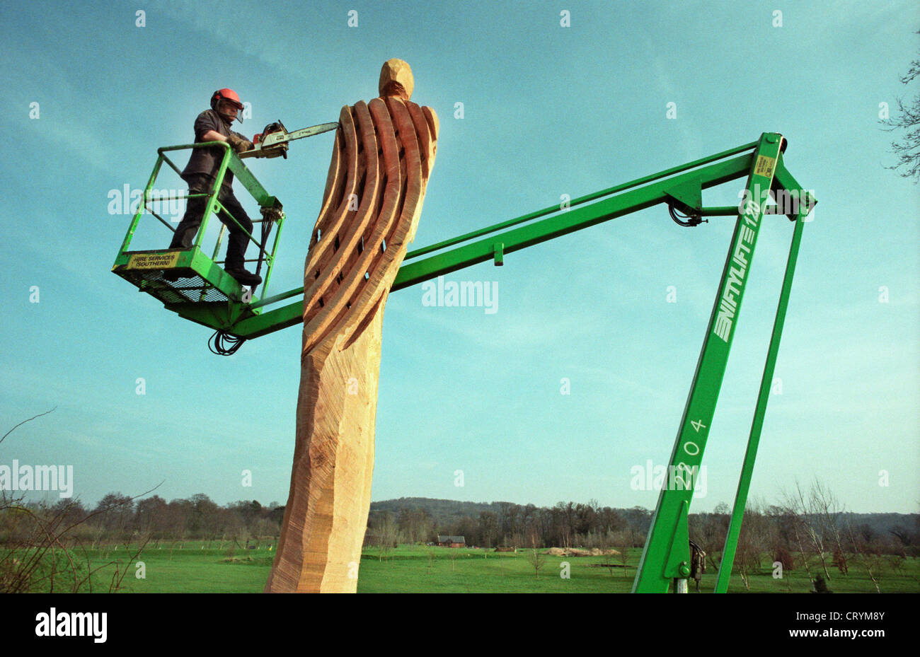 A chainsaw sculptor on the platform of a cherrypicker carving a lattice figure from a dead oak tree in Broadwater Park, Godalming, Surrey, England, UK. Stock Photo