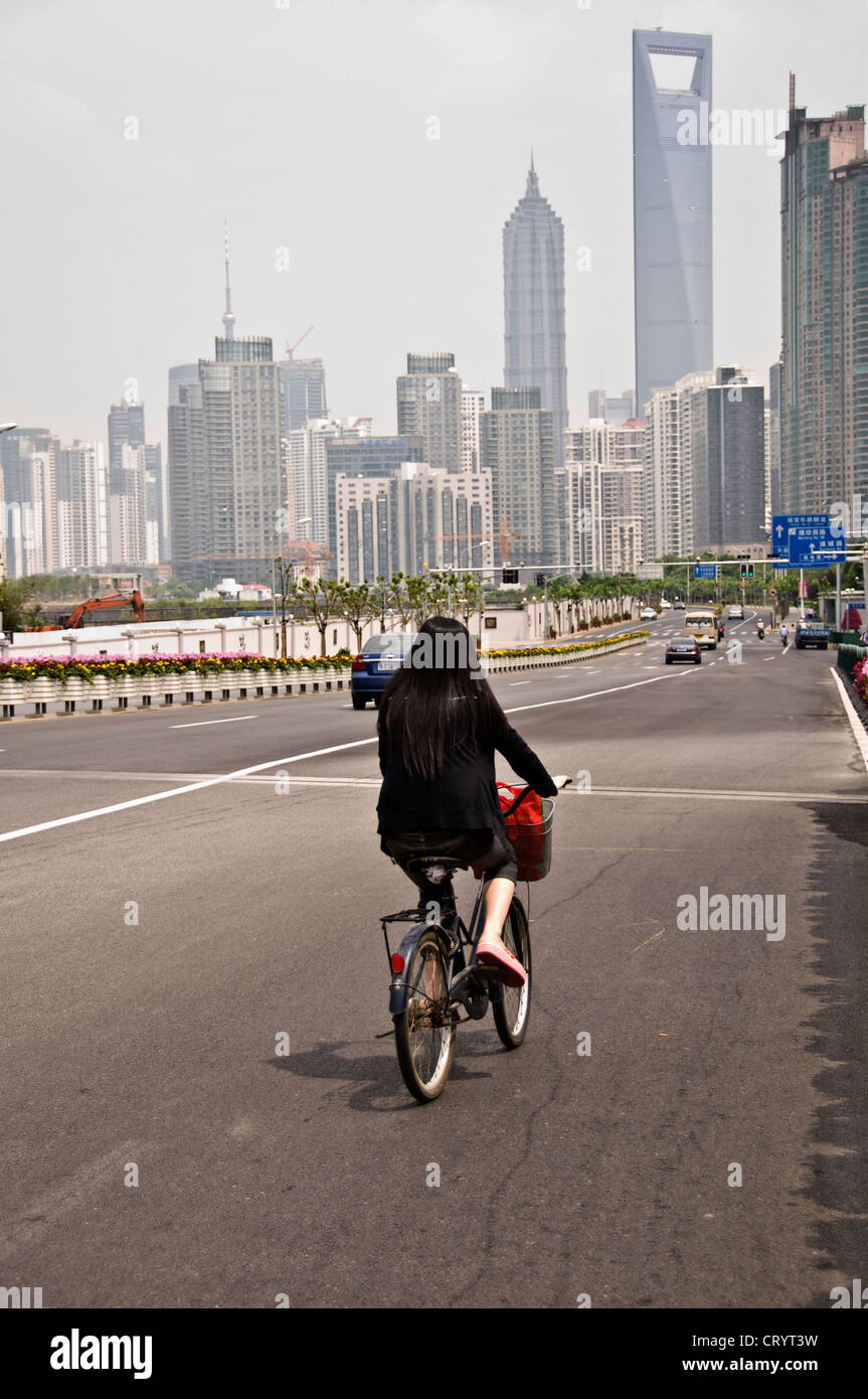 Young woman riding a bicyle on a highway in Shanghai, going toward the towers of Pudong Lujiazui, Jinmao and SWFC - China Stock Photo