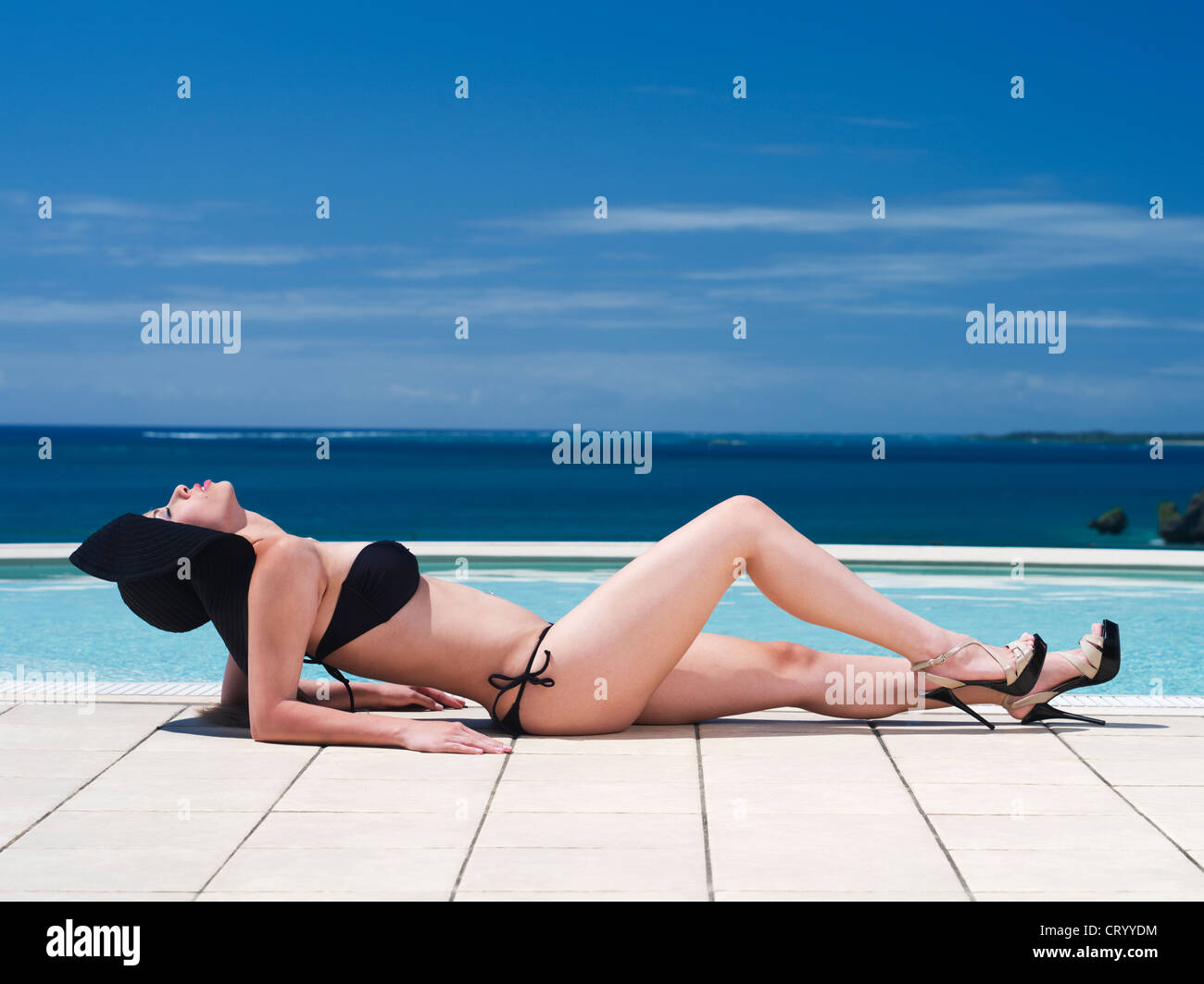 Beautiful Brazilian woman by the pool in bikini, high heels and sun hat. Stock Photo