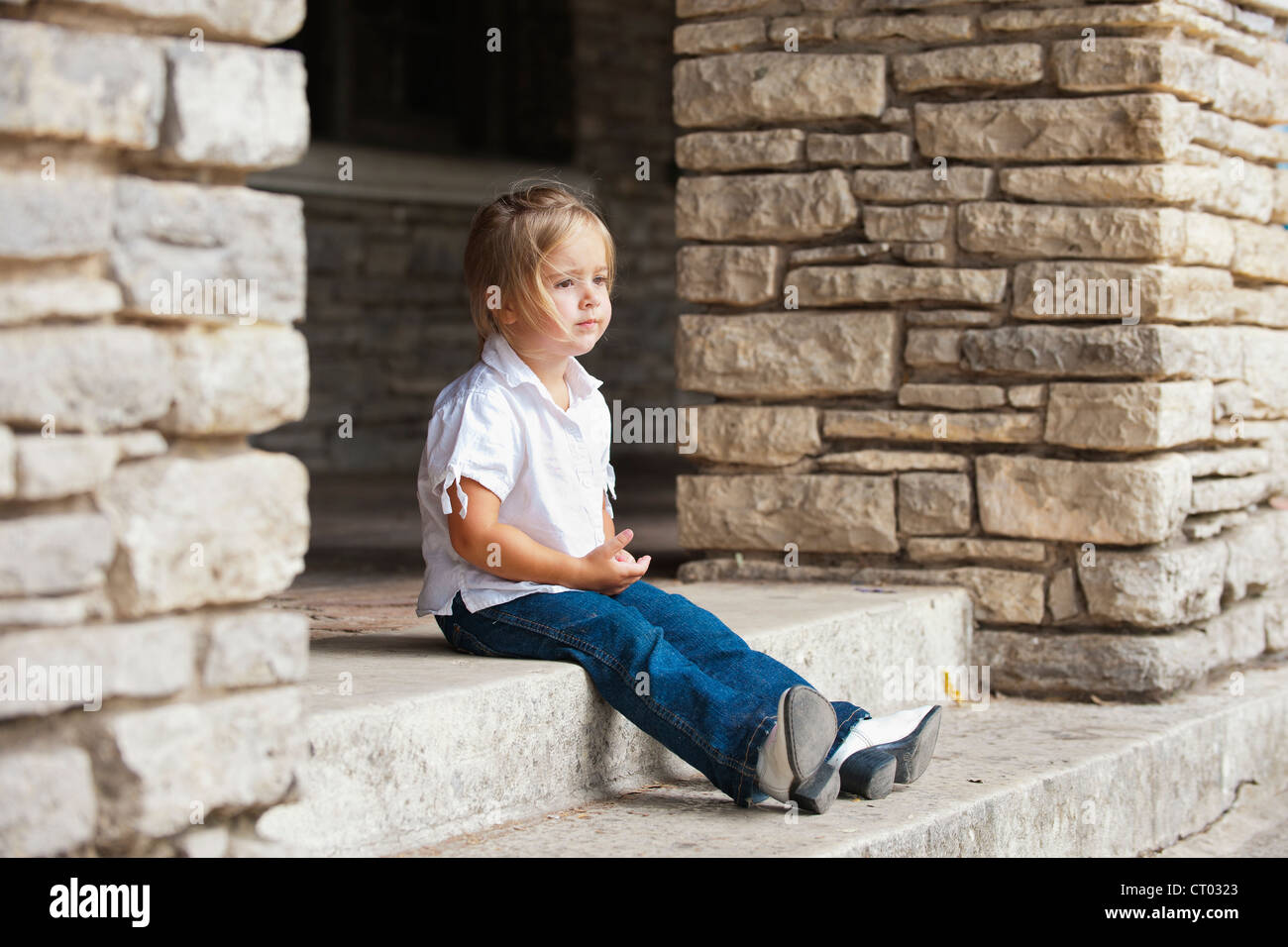 Cute little girl of 4 years seems to be left alone sitting on stairs of historical building Stock Photo