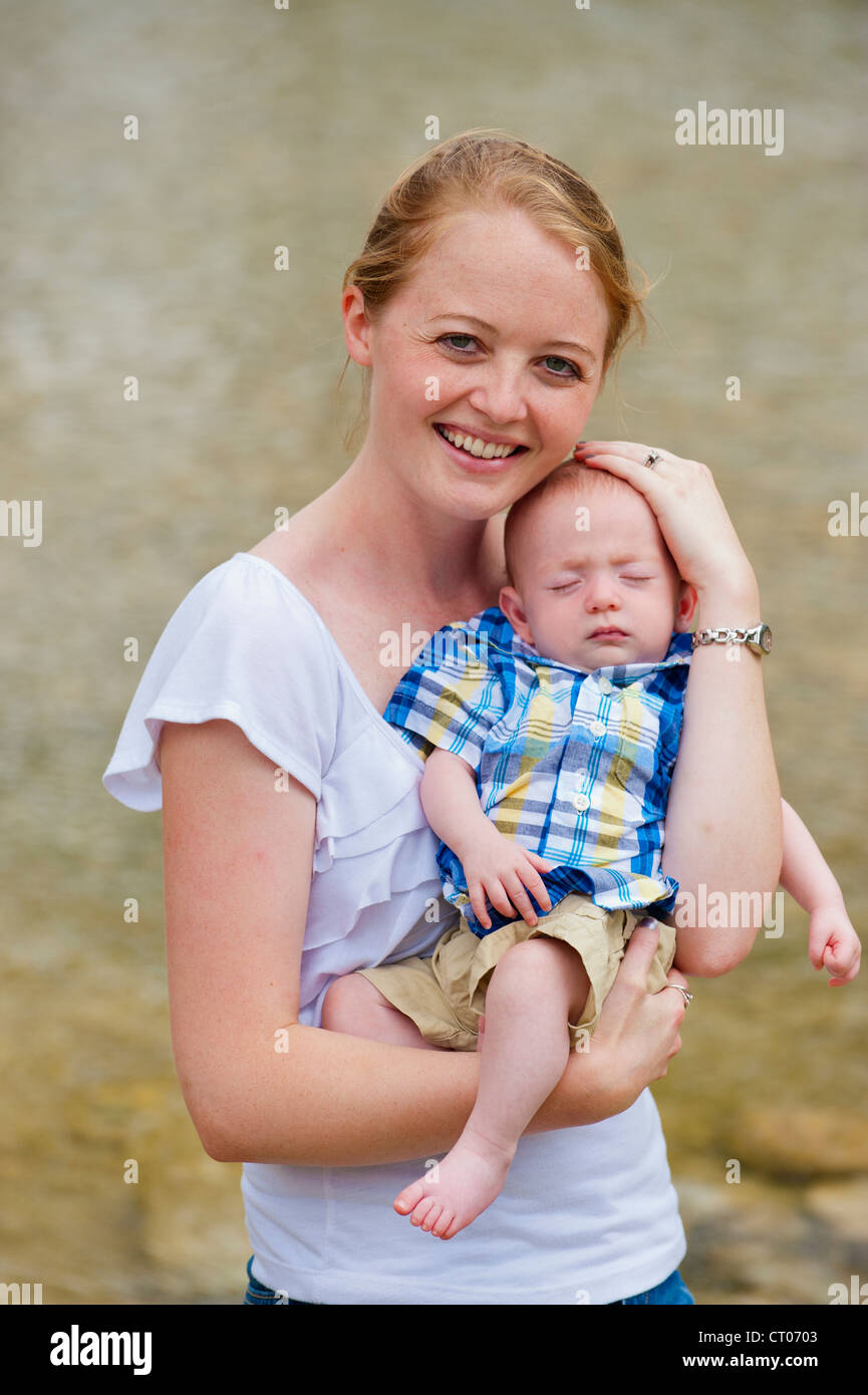 Young happy mother holding her baby boy while protecting his head with her hand Stock Photo