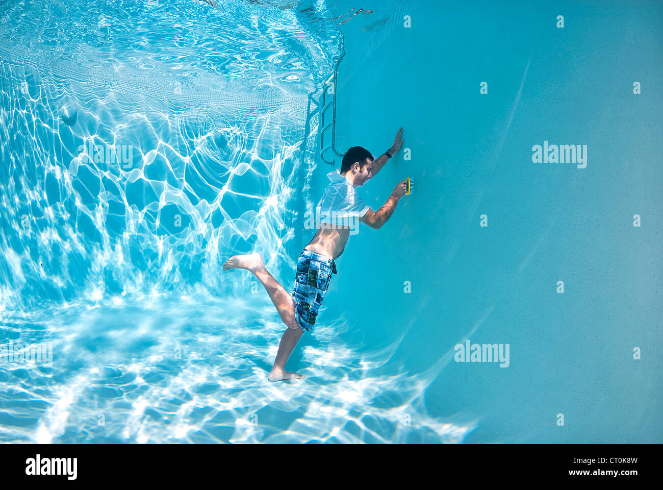 Young man is cleaning the swimming pool from underwater with a brush Stock Photo