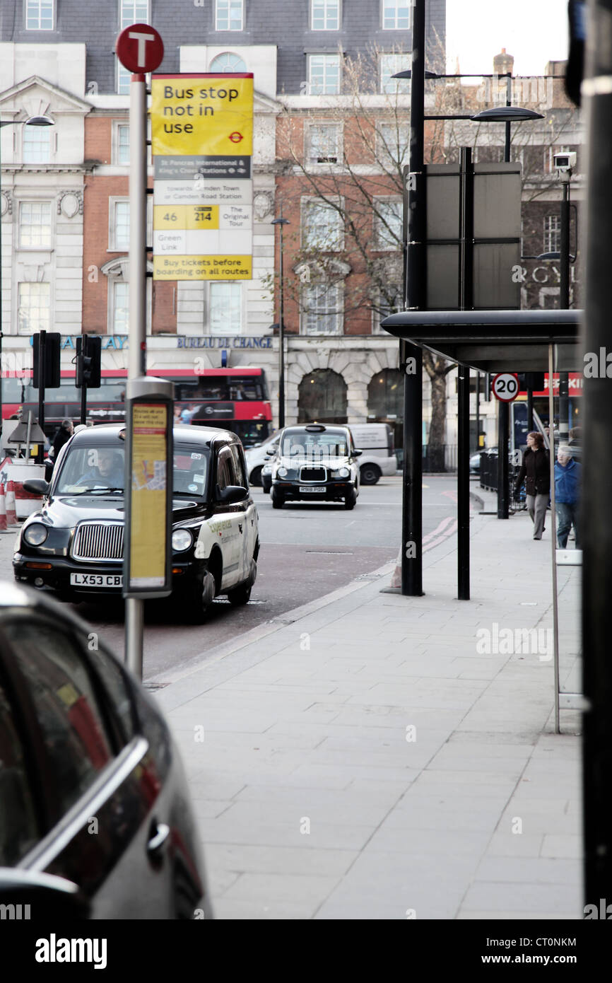 It's a photo of a bus stop in the street of London. We can see cabs and double deck buses on the roads. Stock Photo