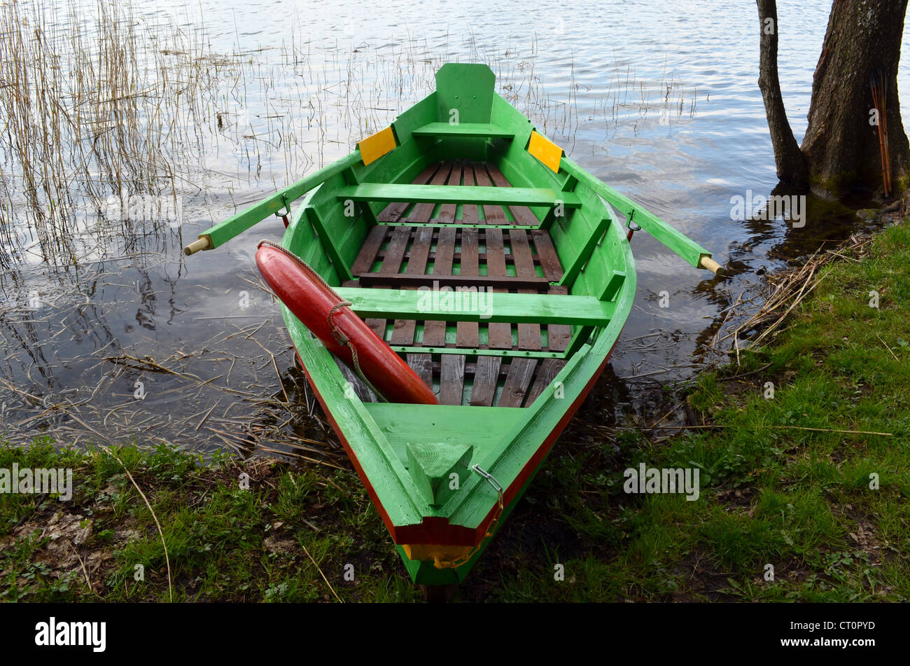 Rowing wooden boat near lake shore and red life saver resque circle in it. Stock Photo