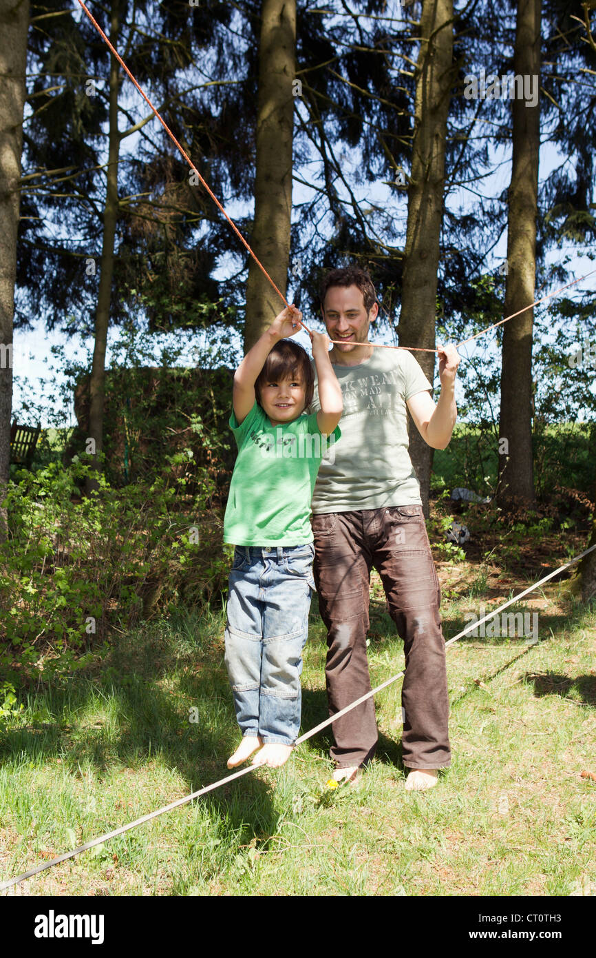 Father helping son walk on tight rope Stock Photo