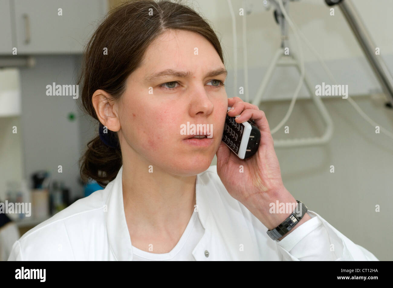 A young dark-haired doctor in a white coat talking on her mobile telephone. Stock Photo