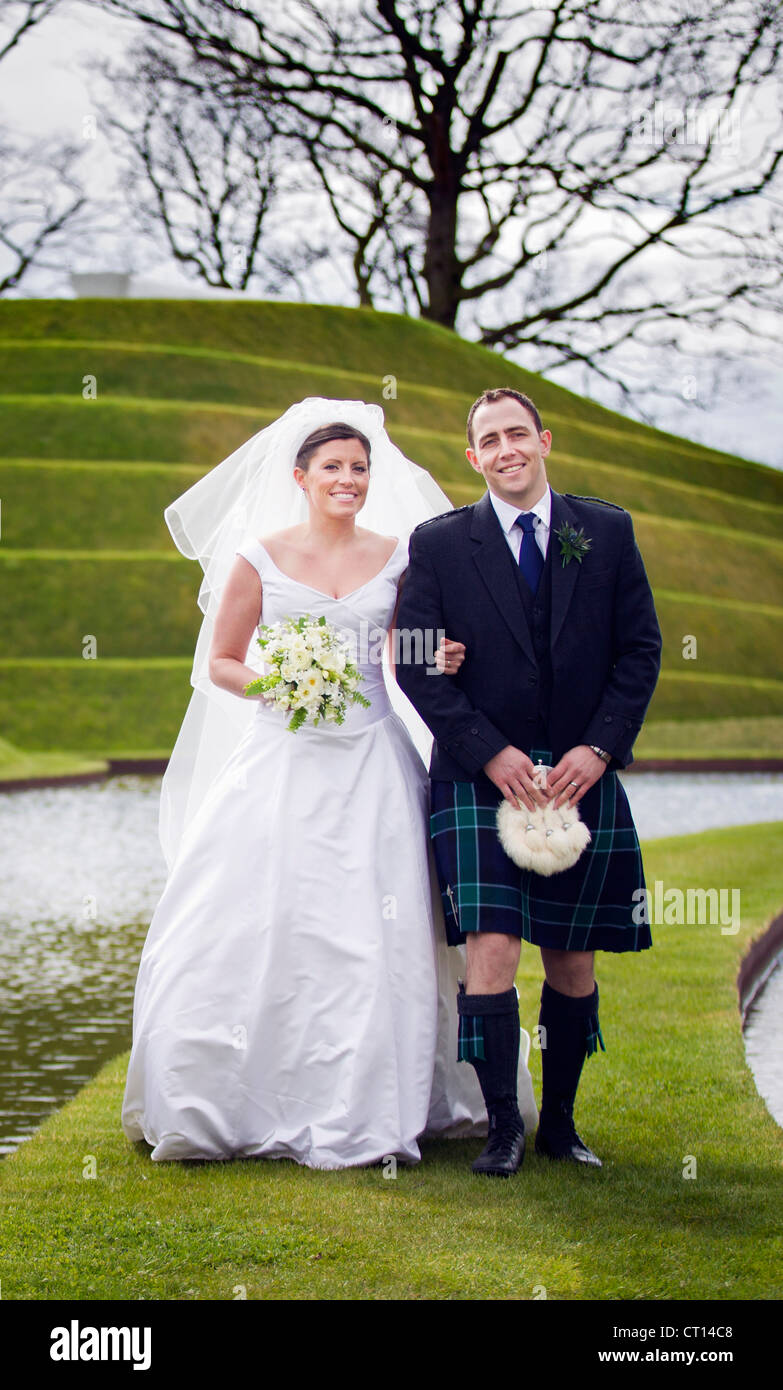 Newlywed couple walking on grassy bridge Stock Photo