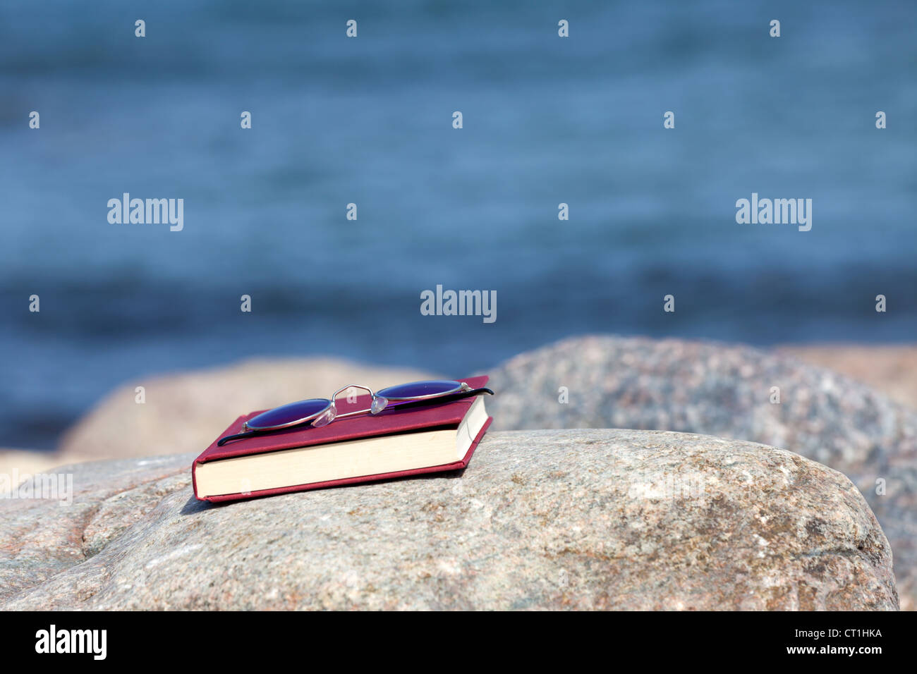 Closed Book with dark tinted sun glasses lies on a rock on the beach Stock Photo