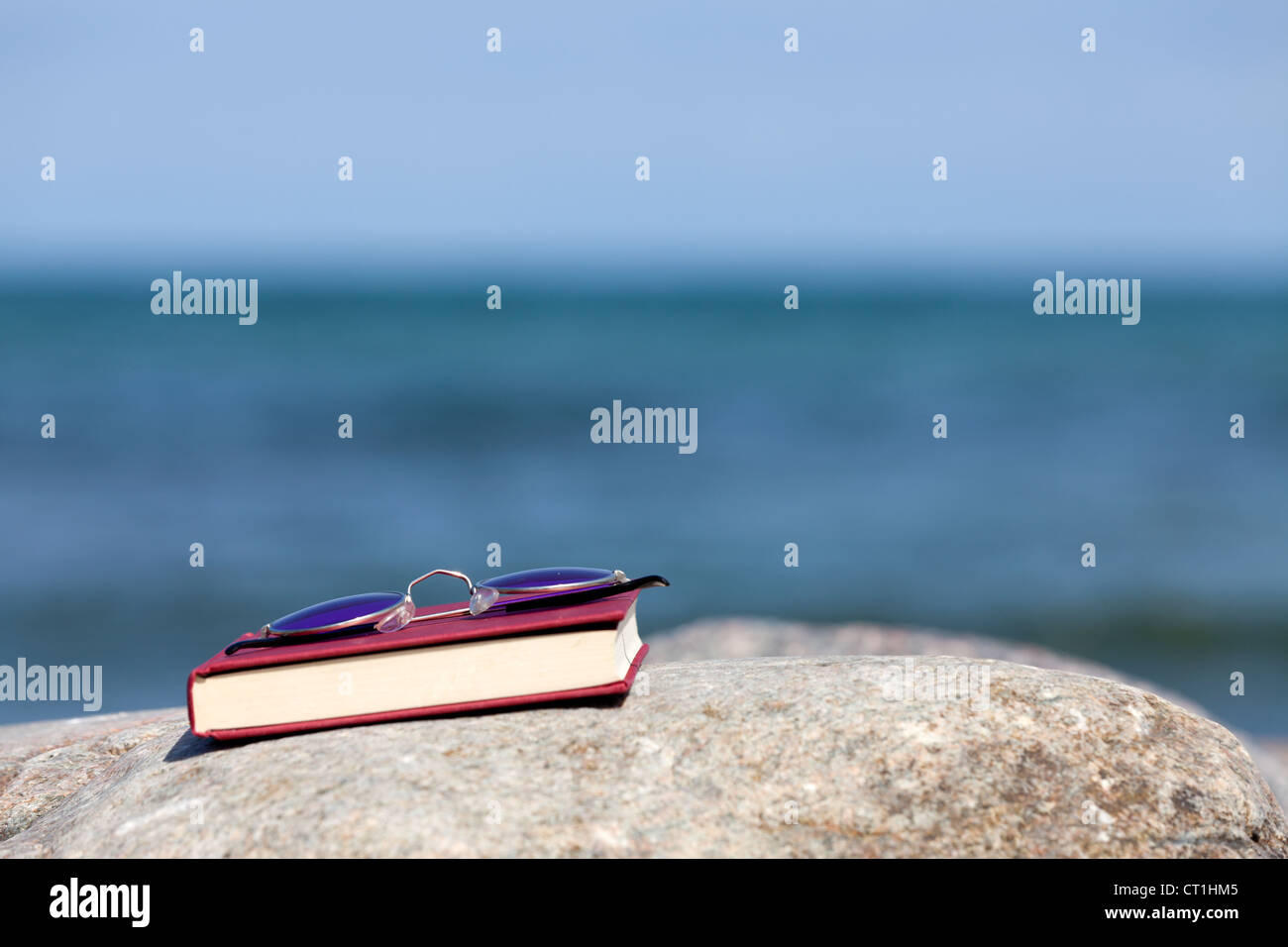 Closed Book with dark tinted sun glasses lies on a rock on the beach Stock Photo