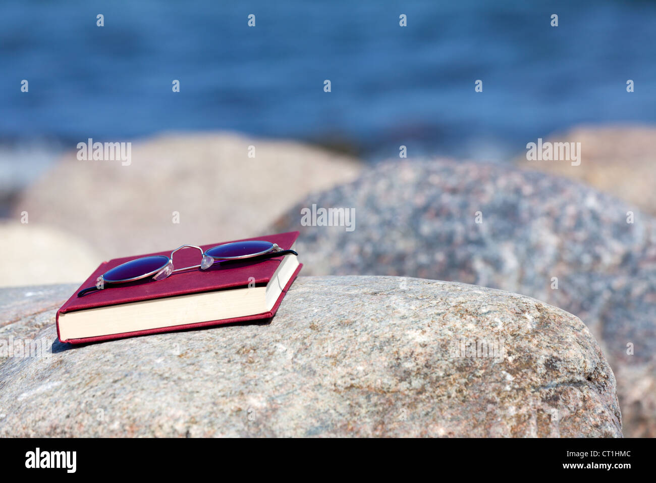 Closed Book with dark tinted sun glasses lies on a rock on the beach Stock Photo