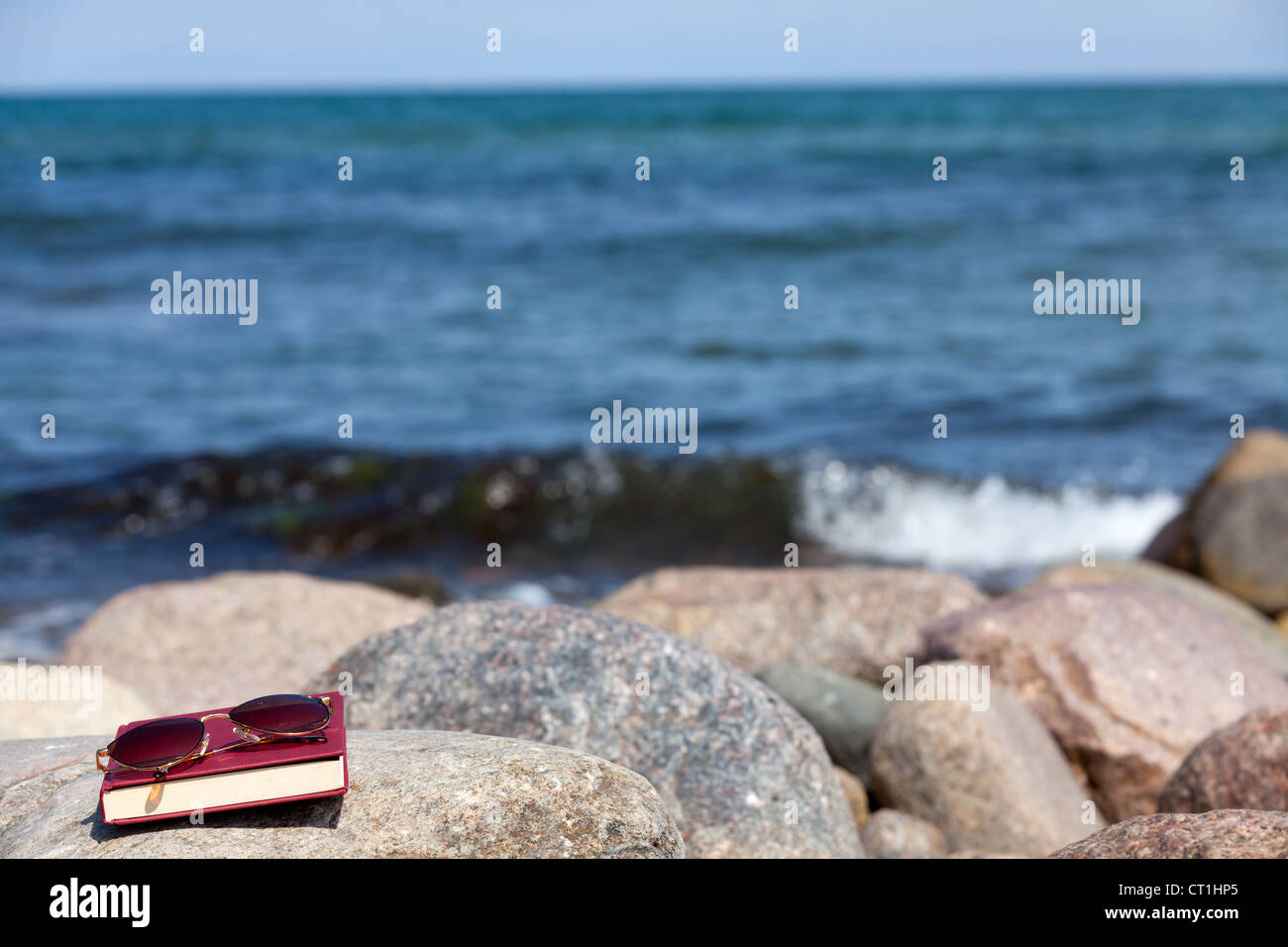 Closed Book with dark tinted sun glasses lies on a rock on the beach Stock Photo