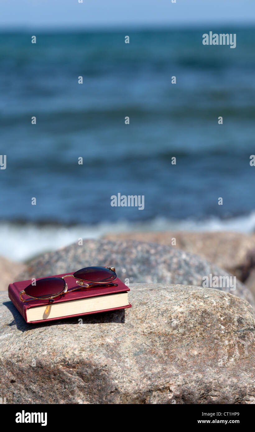 Closed Book with dark tinted sun glasses lies on a rock on the beach Stock Photo