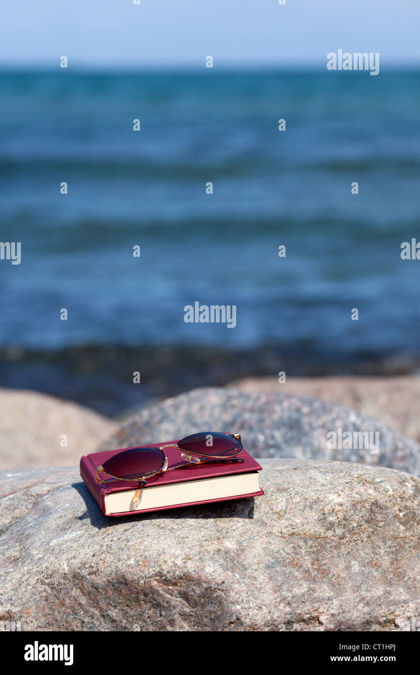 Closed Book with dark tinted sun glasses lies on a rock on the beach Stock Photo