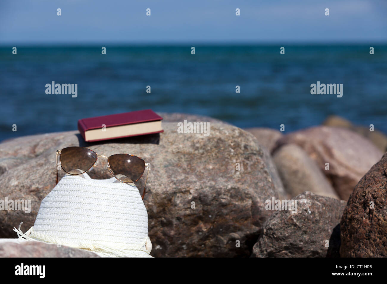 Closed Book with sun glasses and a straw hat lies on a rock on the ...