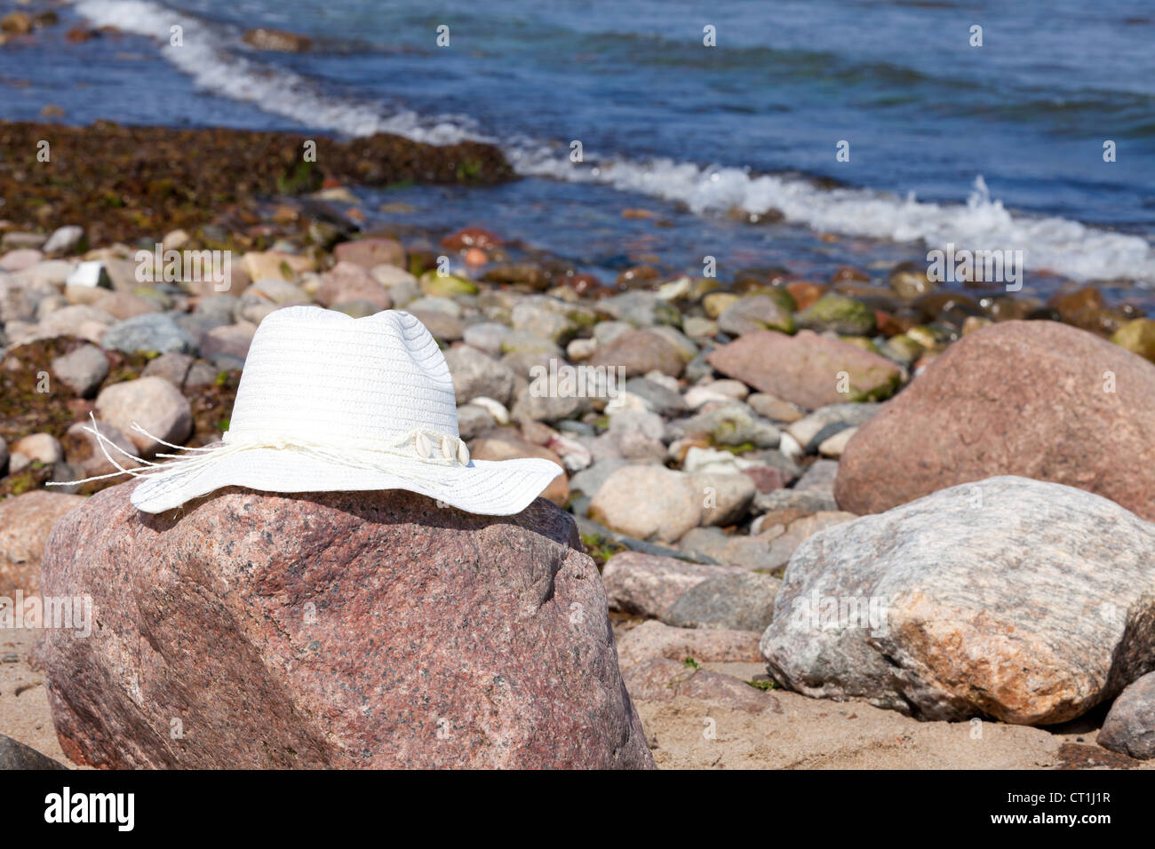 An white straw hat lies on a rock on the beach Stock Photo - Alamy
