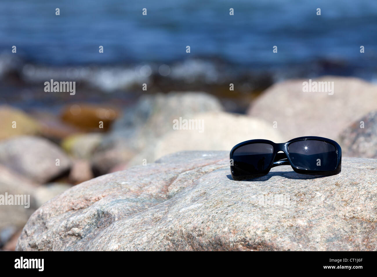 Sunglasses with dark tinted glasses lies on a rock on the coast Stock Photo