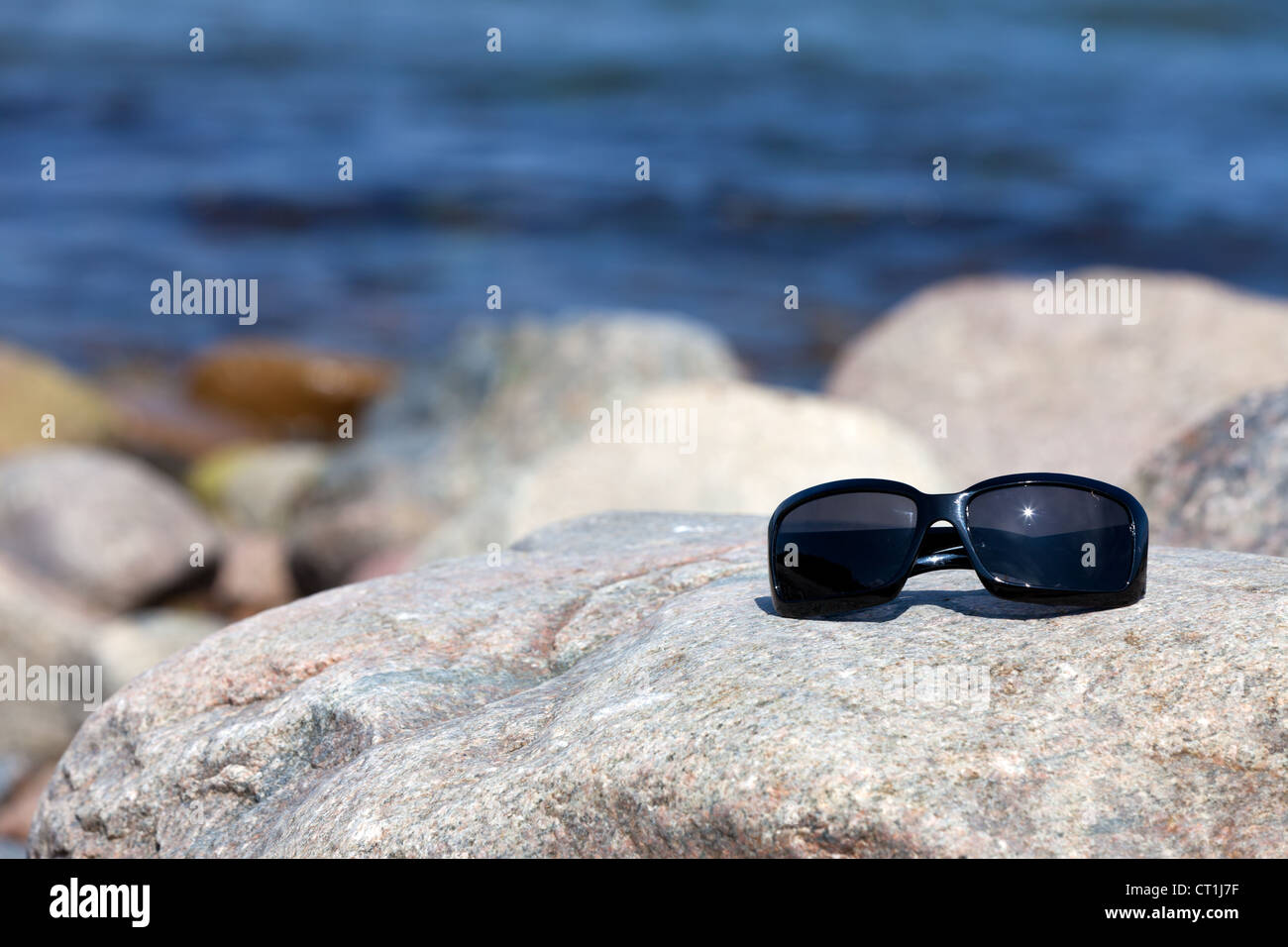Sunglasses with dark tinted glasses lies on a rock on the coast Stock Photo