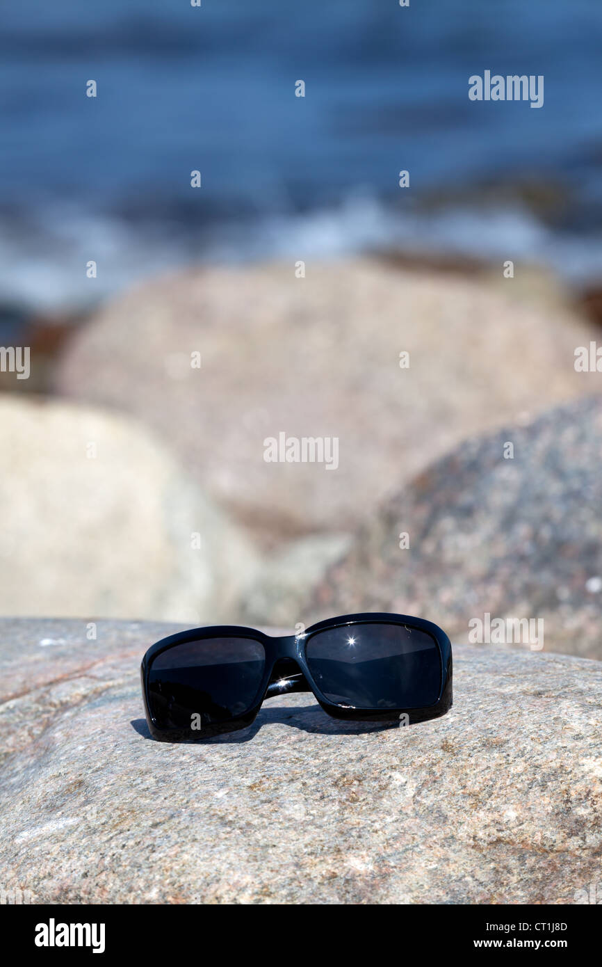 Sunglasses with dark tinted glasses lies on a rock on the coast Stock Photo