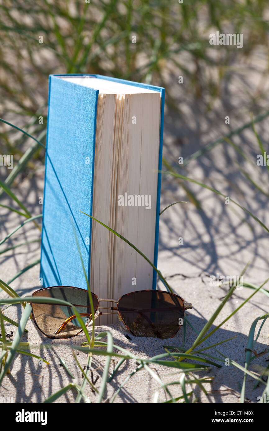 A book with a sunglass lying in the sand in a dune Stock Photo