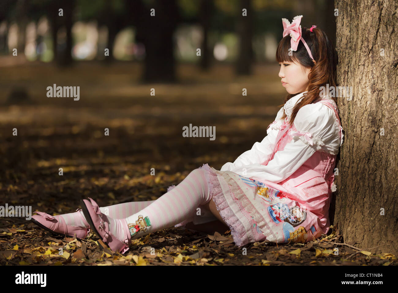 sad japanese lolita leaning against tree in park Stock Photo