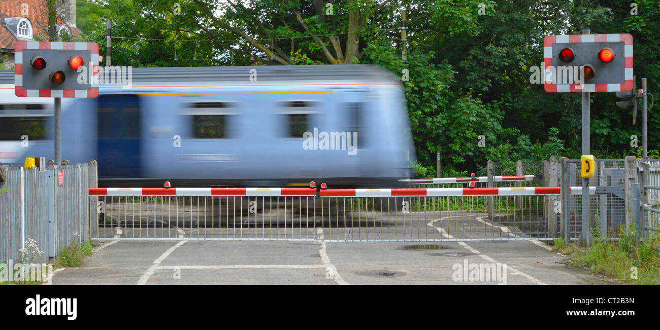 Railway tracks red flashing warning light sign level crossing barrier gates country road passenger train motion blur at Margaretting Essex England UK Stock Photo